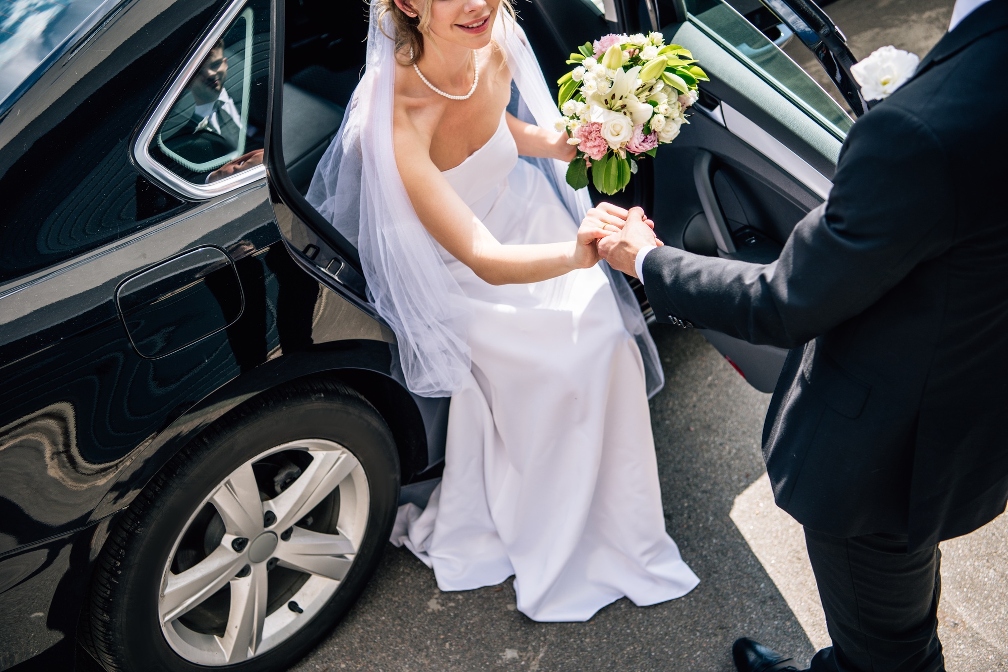 cropped view of bridegroom in suit giving hand to bride with bouquet